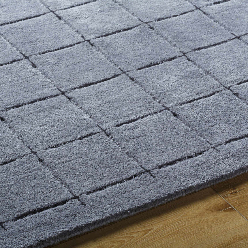 Close up of the hand tufted Sanvi Charcoal Area Rug. The rug has a geometric square pattern and a soft wool texture. Texture