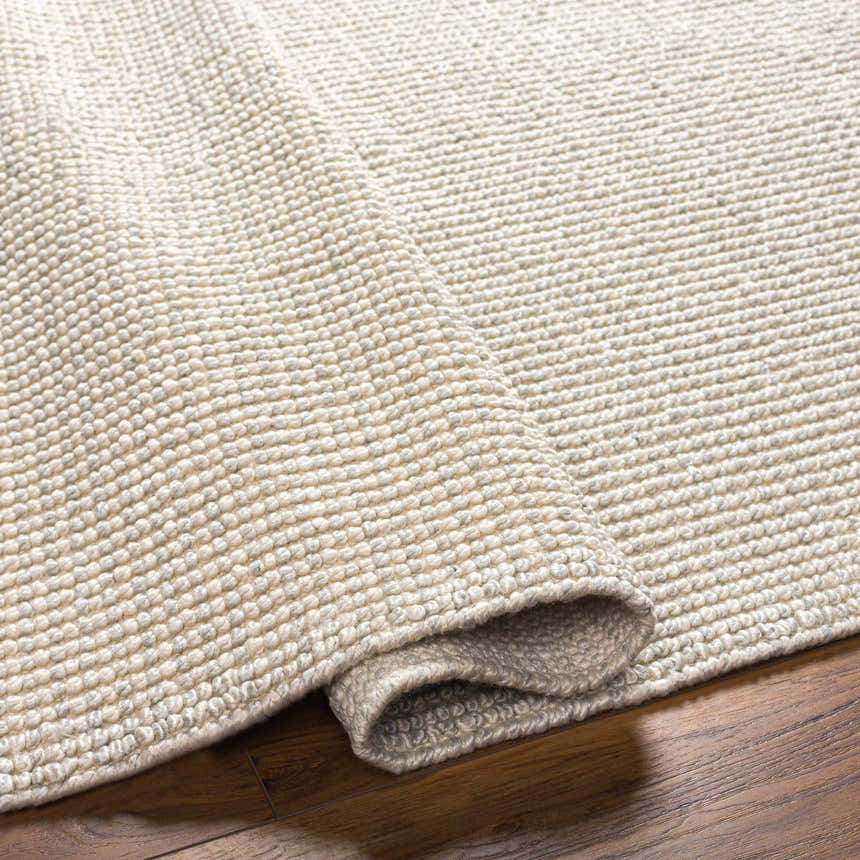 Close-up of the hand-woven Edith Premium Rug in beige and gray, showing the textured, looped pile construction. Fold