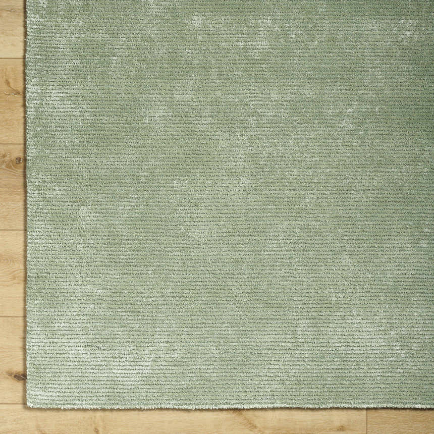 Close-up of the sage Helio Area Rug showing its subtle horizontal texture and soft viscose material on a wood floor. Corner