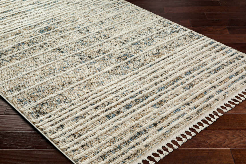 Close-up of Miyu Brown Area Rug showing beige, brown, and blue tones with a contemporary striped pattern and fringe detail on dark wood floor. Corner