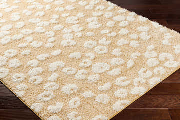 Close-up of the Hirsi Area Rug showing a shag texture with an abstract white pattern on a camel background. Corner