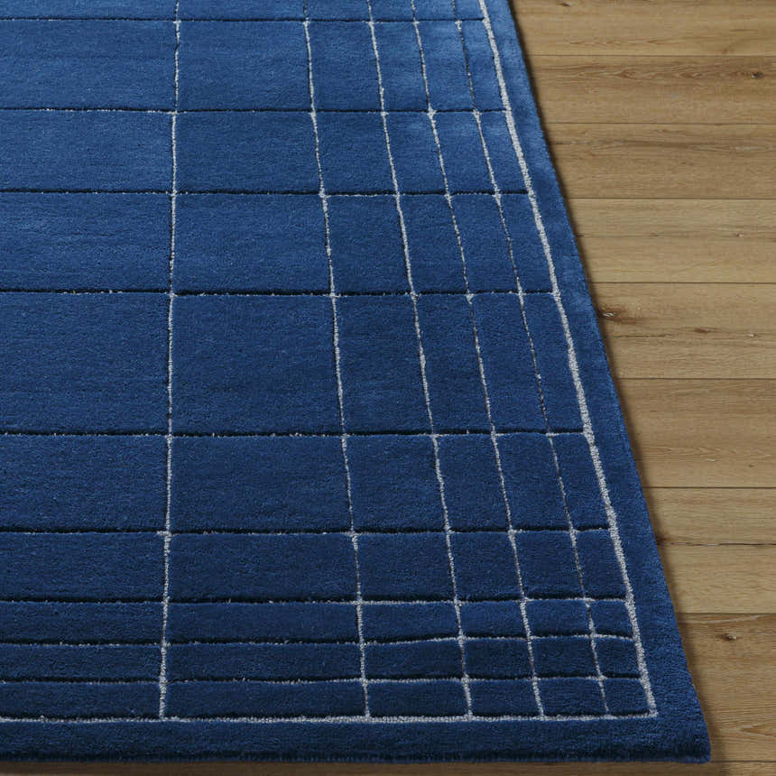 Close-up of the Sedna Navy Wool Area Rug showing its navy color and geometric grid pattern on wood floor. Front