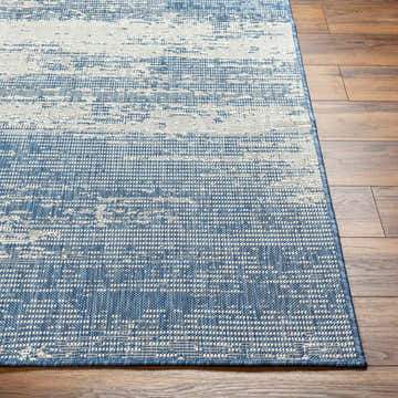Close-up of the Cline Blue Area Rug showing its denim and white contemporary pattern and textured weave on wood floors. Front