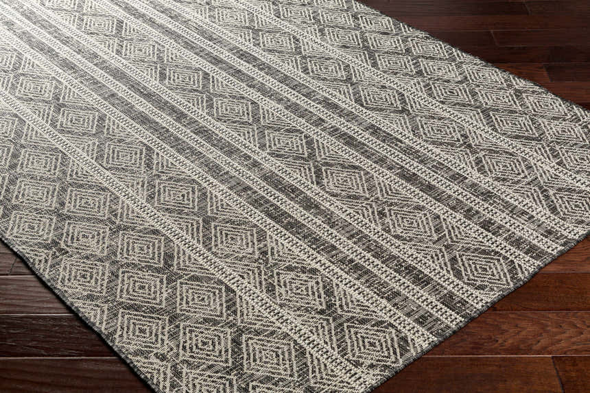 Close-up of the Gavin Nutmeg Area Rug showing a geometric diamond pattern in beige, bone, and gray on dark wood floors. Corner