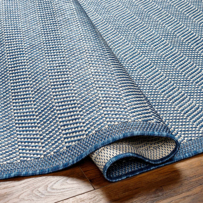 Close-up of the Genet Blue Area Rug showing its woven texture and geometric pattern in denim and white hues. Fold