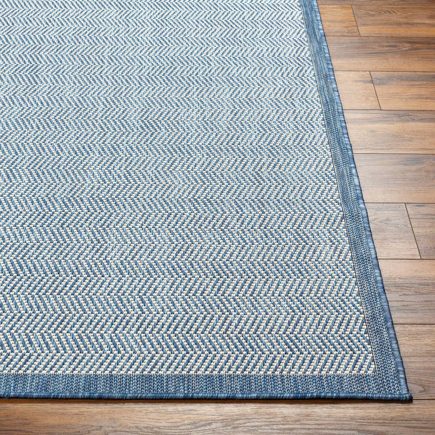 Close-up of the Genet Blue Area Rug showing its denim blue and white herringbone pattern and textured weave. Front