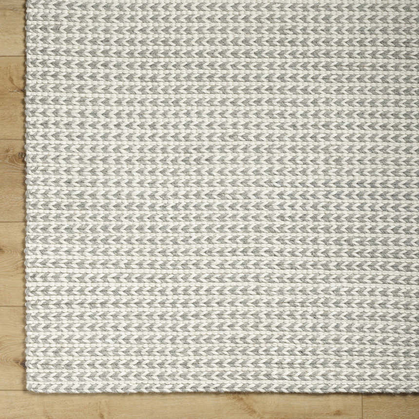 Close up of the hand woven Lenci Bone Area Rug showing beige and bone braided texture on wood floor. Corner
