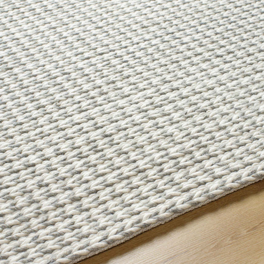 Close up of the hand woven Lenci Bone Area Rug showing its beige and bone braided texture on wood floor. Texture