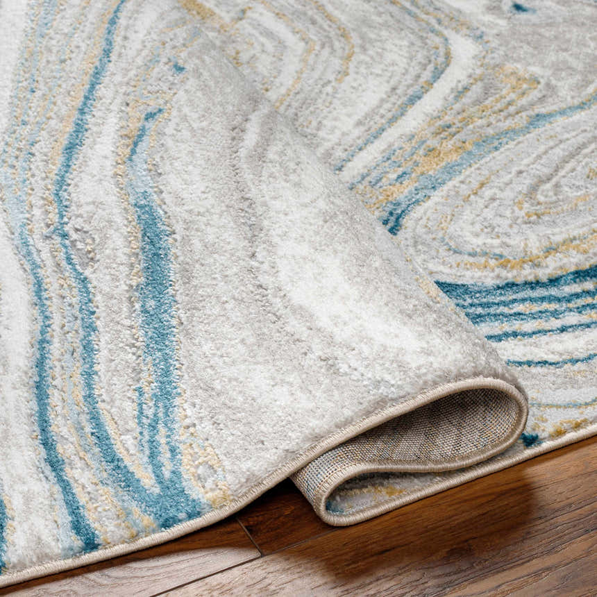 Close-up of the Gregg Silver Gray Marble Area Rug. Features arctic sky blue, camel, and gray marble-like pattern. Fold