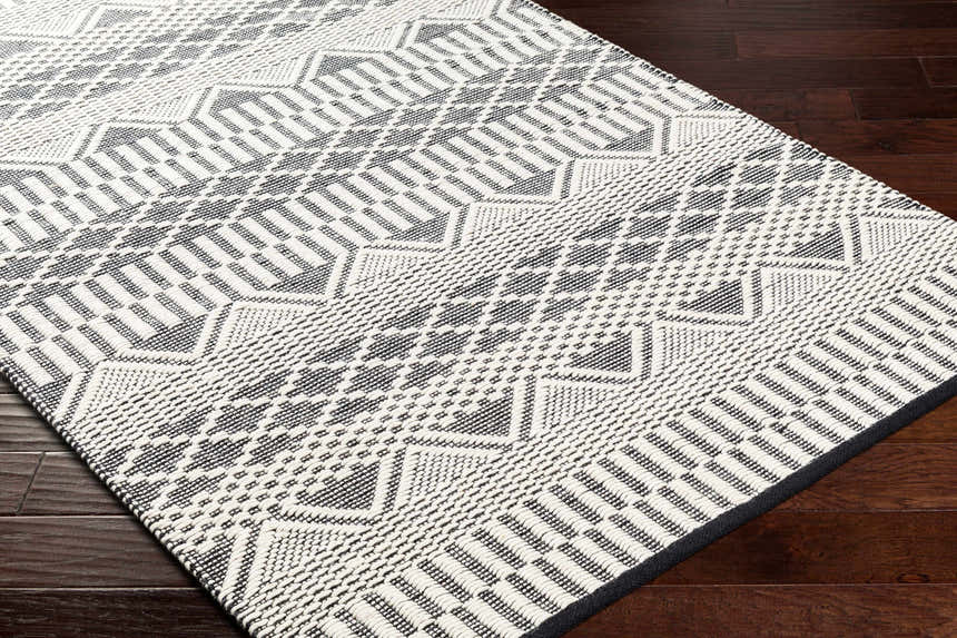 Close-up of the hand woven Carly Area Rug, featuring a geometric pattern in dark gray, nickel, off white, smoke, and taupe. Corner