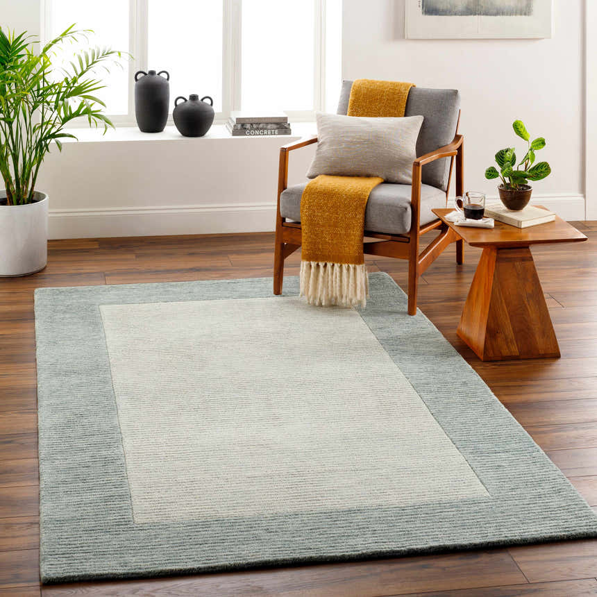 Living room scene with Amadi Green Wool Area Rug, gray chair, wood side table, and plants. Roomscene-Rectangle