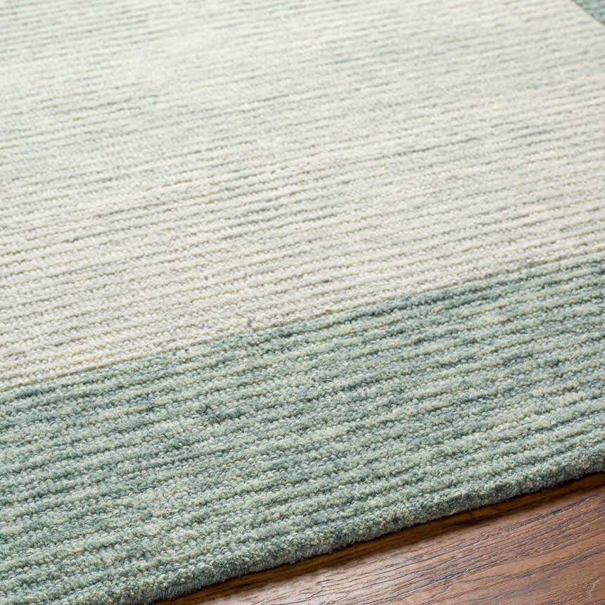 Close-up of the hand-tufted Amadi Green Wool Area Rug showing texture and color variations on wood flooring. Texture