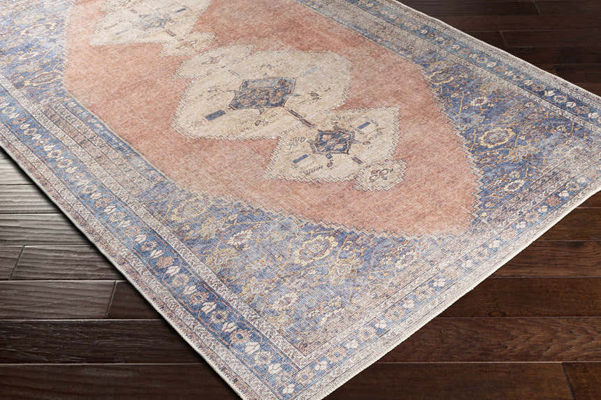 Close-up of the Stakeford Washable Area Rug showing light blue, peach, and tan colors on dark wood floors. Corner