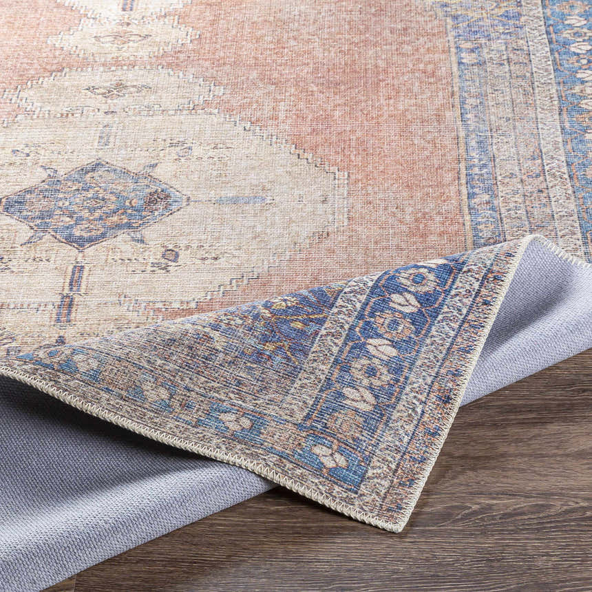 Close-up of the Stakeford Washable Area Rug showing light blue, gray, peach, and tan tones and intricate design. Fold