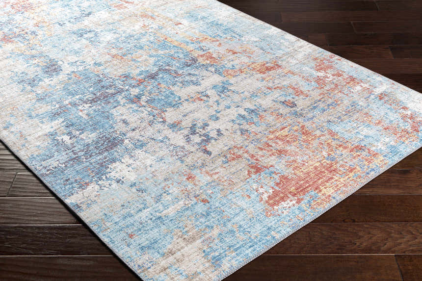 Close-up of the Stallingborough Area Rug showing its abstract pattern in blue, rust, cream, and tan on dark wood floors. Corner