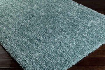 Close-up of the plush, teal Stratford Area Rug. Shag texture on dark wood floor. Corner