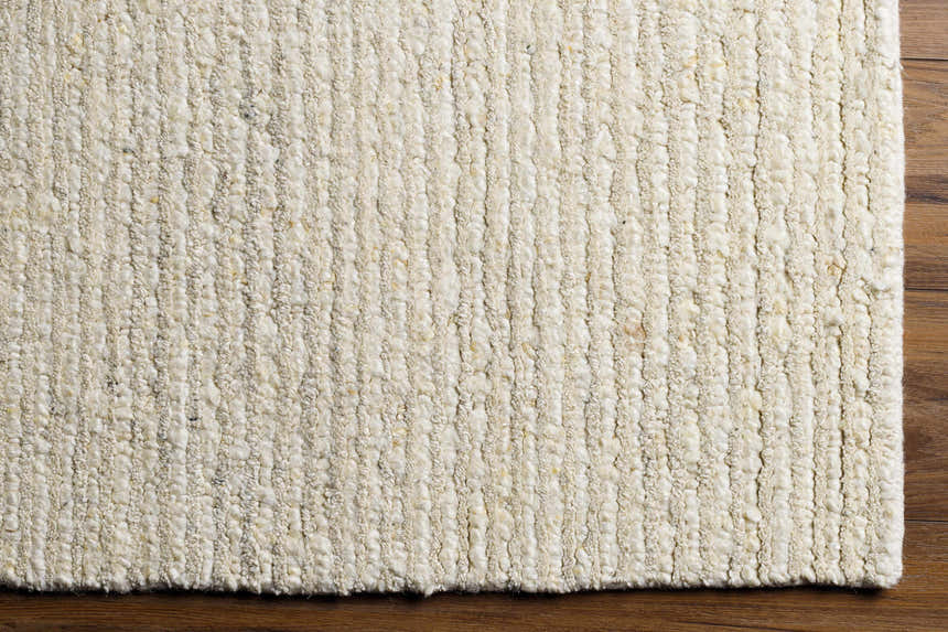 Close-up of the hand woven Chaz Cream Wool Rug showing its textured, Scandinavian design and bone, khaki, and white thatch colors. Corner