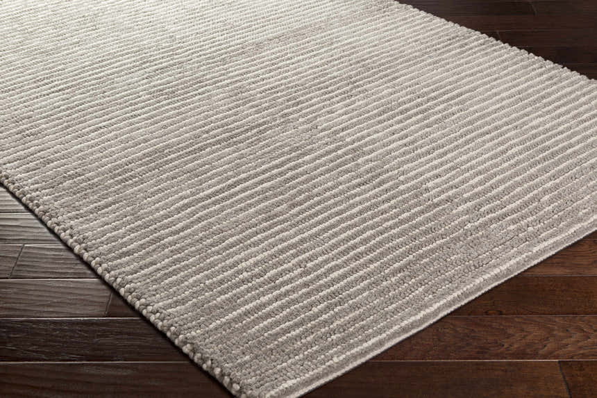 Close-up of the Sula Area Rug. Hand-woven wool rug in cream and gray stripes on a dark wood floor. Corner