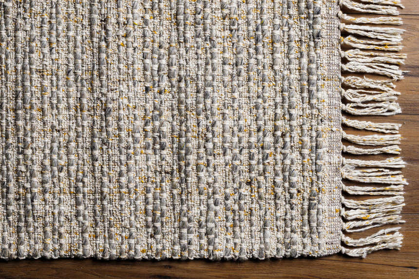 Close-up of the Amiel Beige Rug showing hand woven texture, clay, gray, and peach tones, and knotted fringe detail. Corner