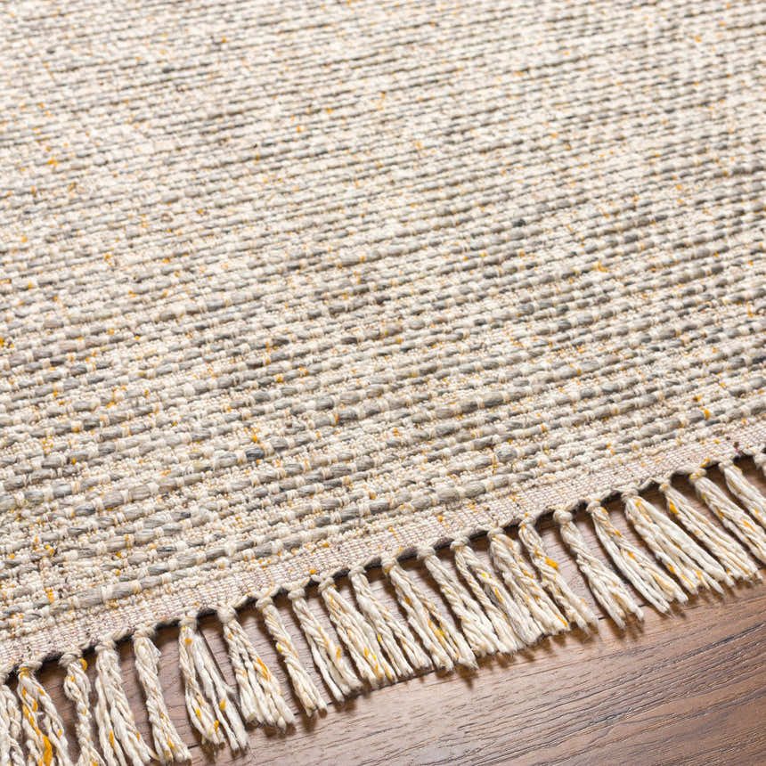 Close-up of Amiel Beige rug showing hand woven texture, neutral colors, and fringe detail on a wood floor. Texture
