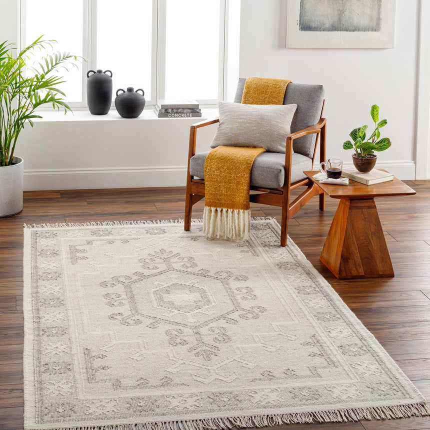 Living room scene with a gray chair, wood side table, and the Afra Area Rug in cloud gray with a traditional pattern. Roomscene-Rectangle