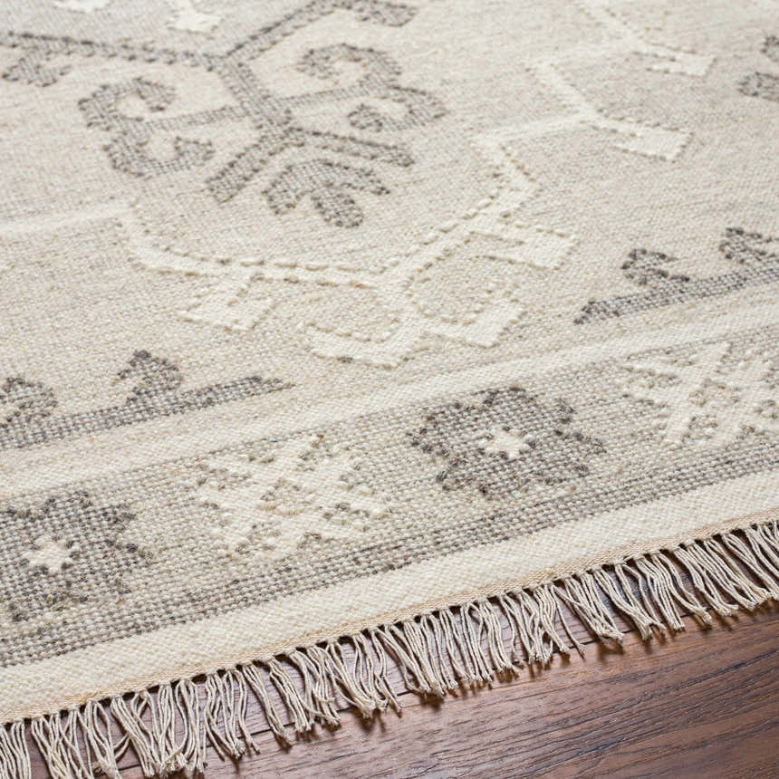 Close-up of the hand woven Afra Area Rug showing its cloud gray, dark gray tones and traditional pattern with fringe. Texture