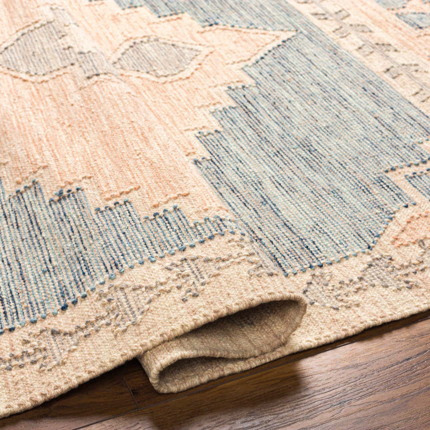 Close-up of the hand-woven Lana Area Rug. Features a geometric pattern in lambswool, light brown, and blue tones. Fold