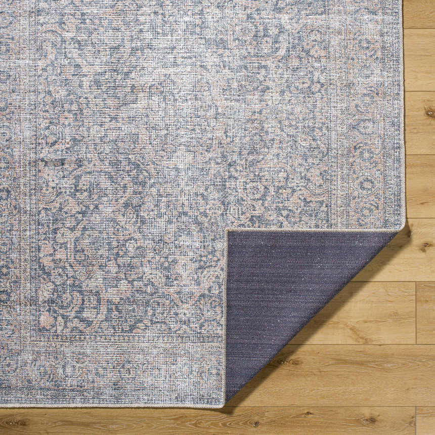 Close-up of the Orsin Washable Area Rug showing its traditional, farmhouse pattern and colors on light wood flooring. Fold