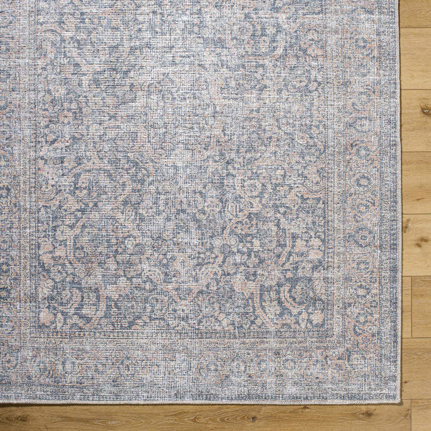 Close up of the Orsin Washable Area Rug showing traditional pattern in blue, peach, and cream on a light wood floor. Corner