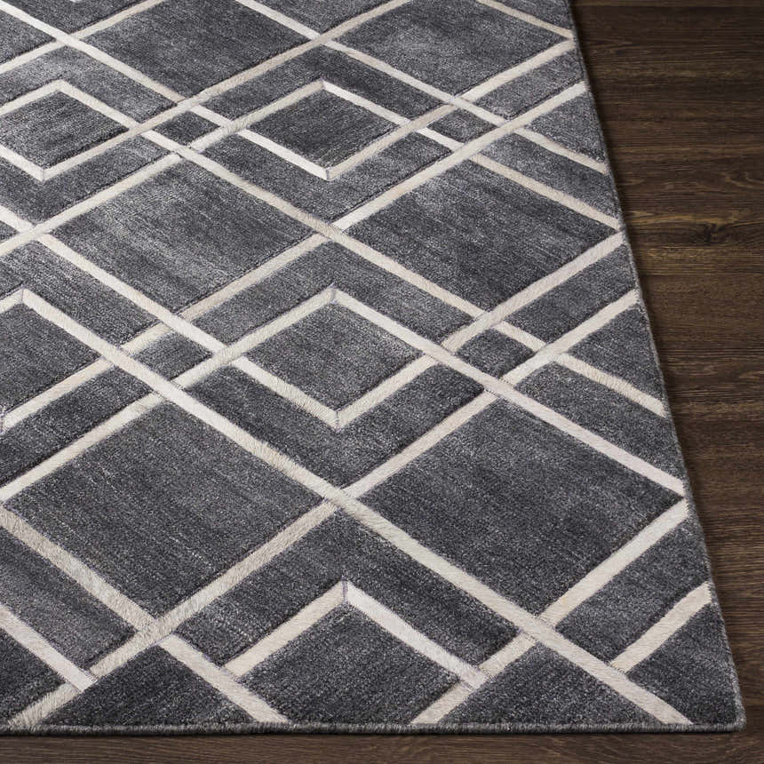 Close-up of the Taclobo Area Rug showing a geometric diamond pattern in black, gray, and light gray on dark wood floor. Front