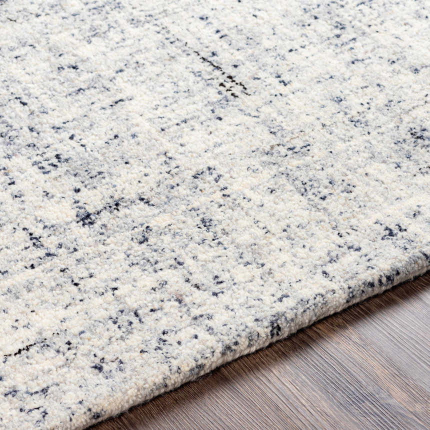 Close-up of the Tanana Area Rug, a hand-tufted wool rug in cream, gray, and black on a wood floor. Contemporary style. Texture