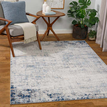 Living room scene with a Texanna Abstract Blue/Gray Area Rug, gray chair, wood table, and monstera plant. Roomscene-Rectangle