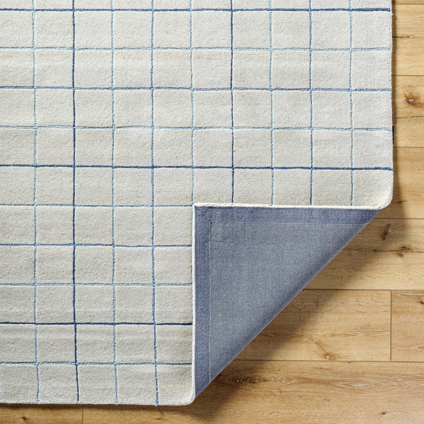 Close-up of Toshi Beige Grid Wool Rug showing blue grid pattern, wool texture, and rug backing on wood floor. Fold