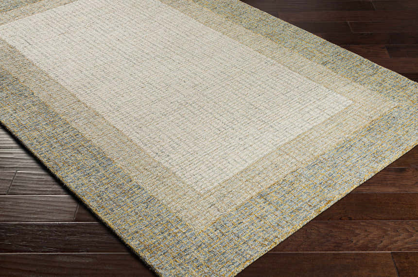 Close-up of the hand-tufted Tandayag Area Rug. Cream center with light beige and dusty sage striped border on dark wood floors. Corner