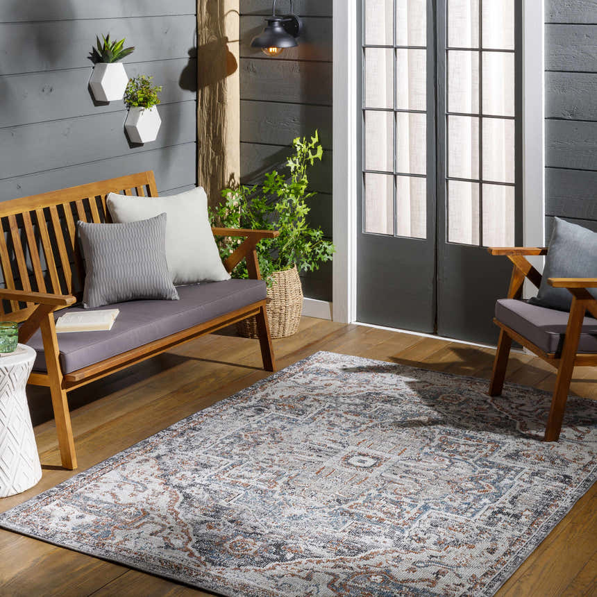 Outdoor patio scene with a Tongala Indoor & Outdoor Rug in beige, blue, and brick red, styled with a wooden bench and chairs. Roomscene-Rectangle