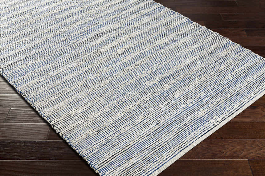 Close-up of the hand-woven Totolan Area Rug. Beige, denim, and black jute stripes on dark wood floor. Coastal Grandmother style. Corner