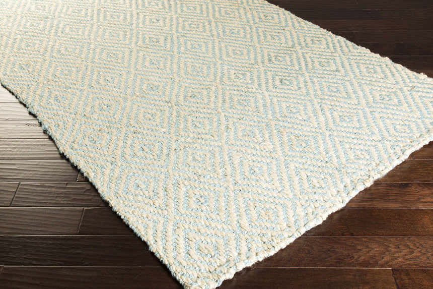 Close-up of the Tyronza Clearance Jute Rug. Hand-woven rug features a cream and sky blue diamond pattern and natural texture. Corner