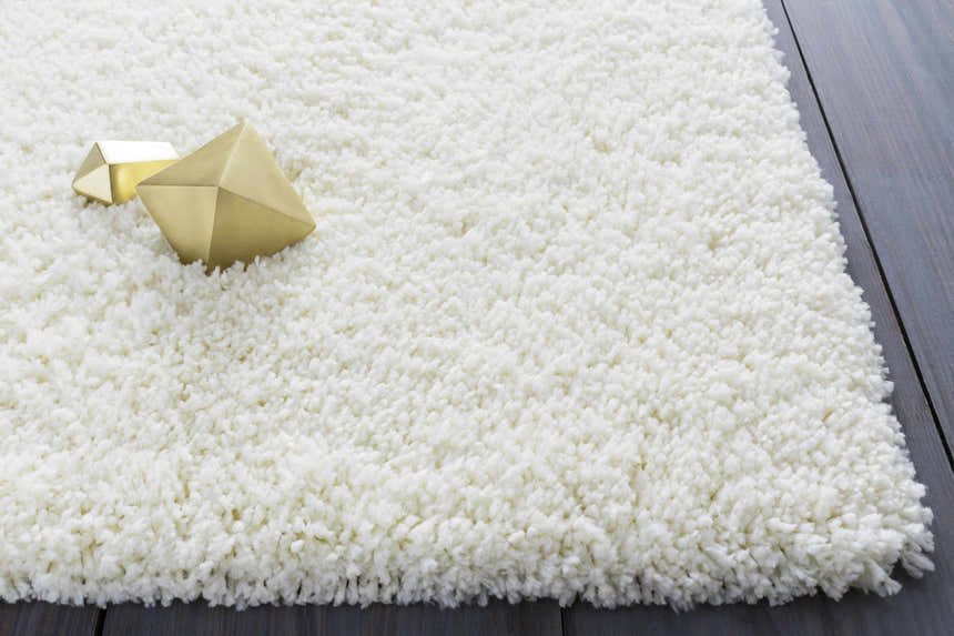 Close-up of the cream Umpire Area Rug, a hand-woven shag rug with geometric gold accents on a dark wood floor. Styleshot