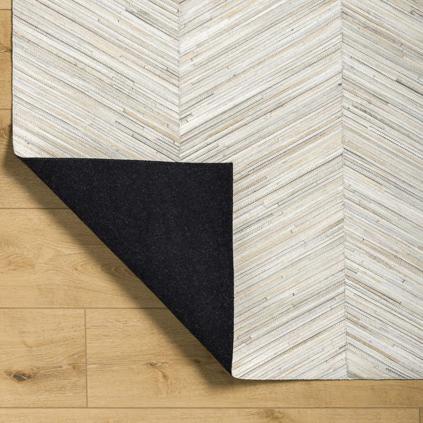Close up of the Upland Premium Rug showing brown, cream, and gray chevron pattern and black backing on wood floor. Fold