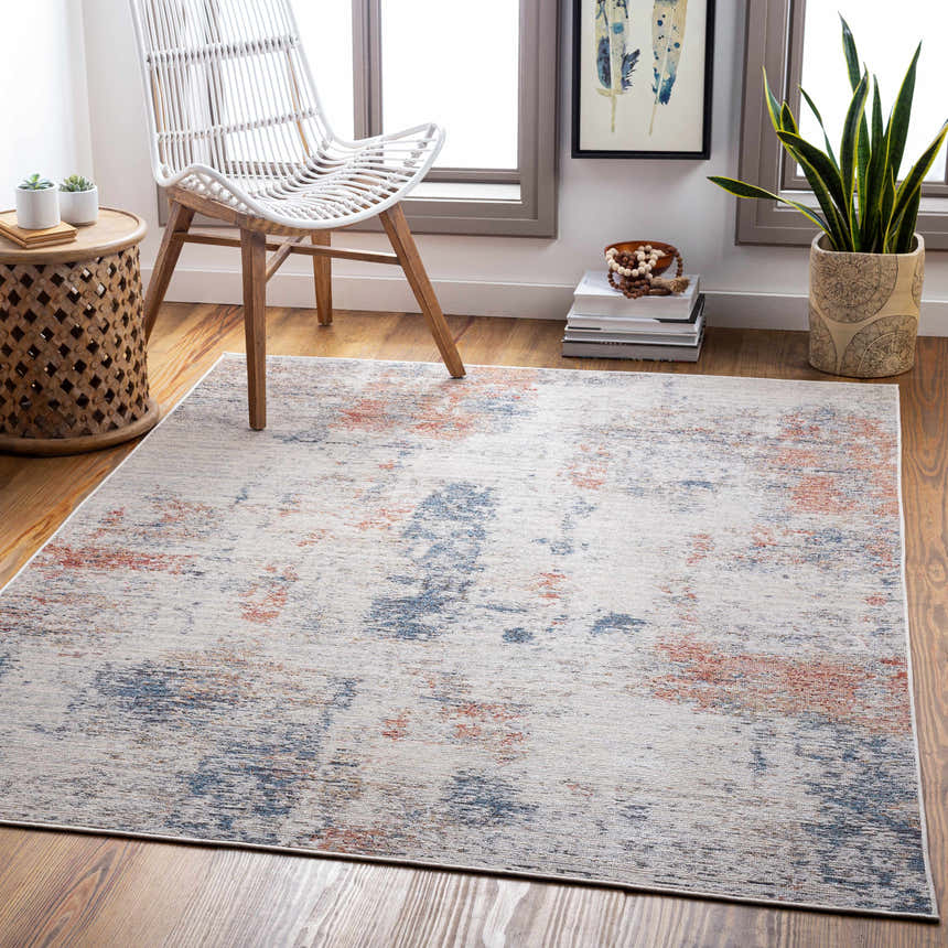 Coastal living room scene with the Upminster Area Rug in brick red, charcoal, and beige. Wicker chair and wood accents. Roomscene-Rectangle