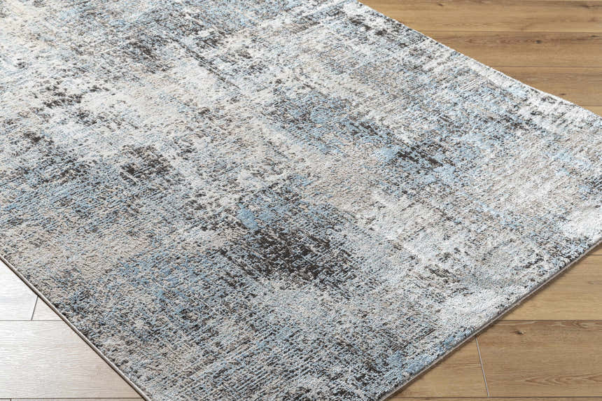 Close-up of Vesna Blue Area Rug showing its abstract Southwestern design, blue, charcoal, and ivory colors, and soft texture. Corner