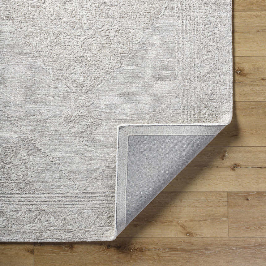 Close-up of the ash-colored Verne Area Rug showing its hand-tufted wool texture and traditional pattern on wood flooring. Fold