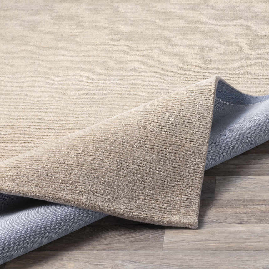 Close-up of the hand loomed Brockton Solid Tan Wool Area Rug showing texture and backing. Fold