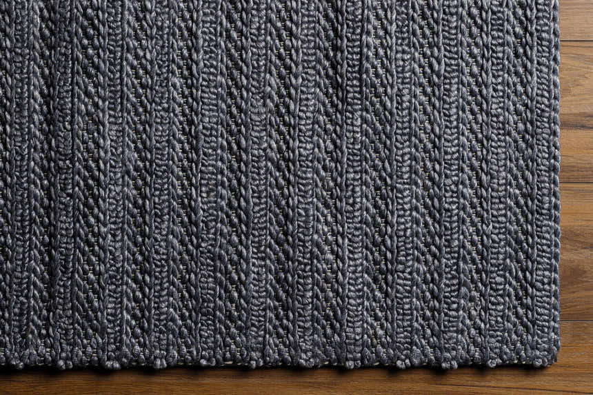 Close-up of the hand woven Warrendale Area Rug. Charcoal gray viscose rug with a subtle herringbone pattern and natural texture. Corner