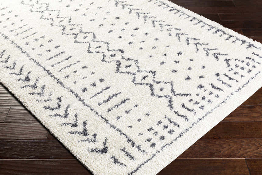 Close up of the Wedowee Area Rug showing its white shag texture and gray geometric, bohemian-inspired pattern. Corner