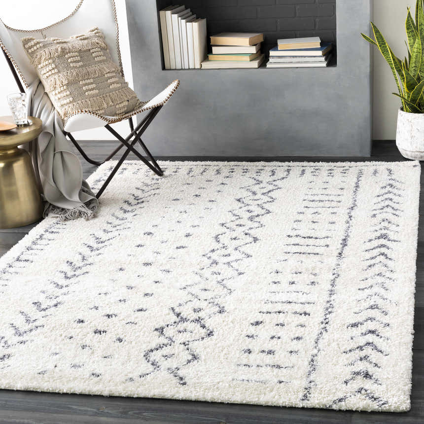 Living room scene with a white and gray Wedowee Area Rug, modern chair, gold side table, and fireplace. Roomscene-Rectangle
