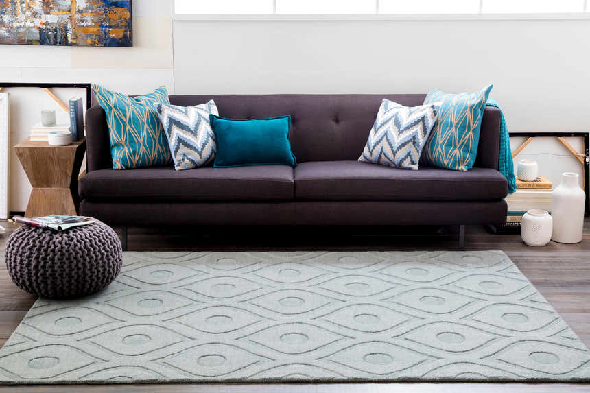 Living room scene with a light gray Welaka Eye Pattern Wool Rug, dark sofa, and teal and gray pillows. Roomscene-Rectangle