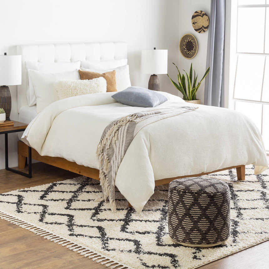 Bedroom scene with a Bohemian style Ogallah Area Rug, white bedding, and a patterned ottoman. Styleshot