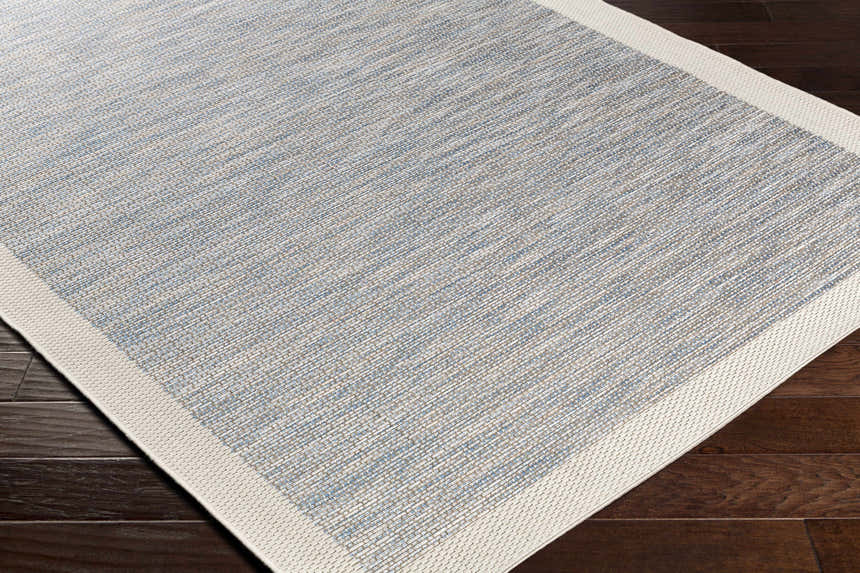 Close-up of the Wishon Area Rug. Blue, cream, and taupe woven texture with a cream border on dark wood floors. Corner