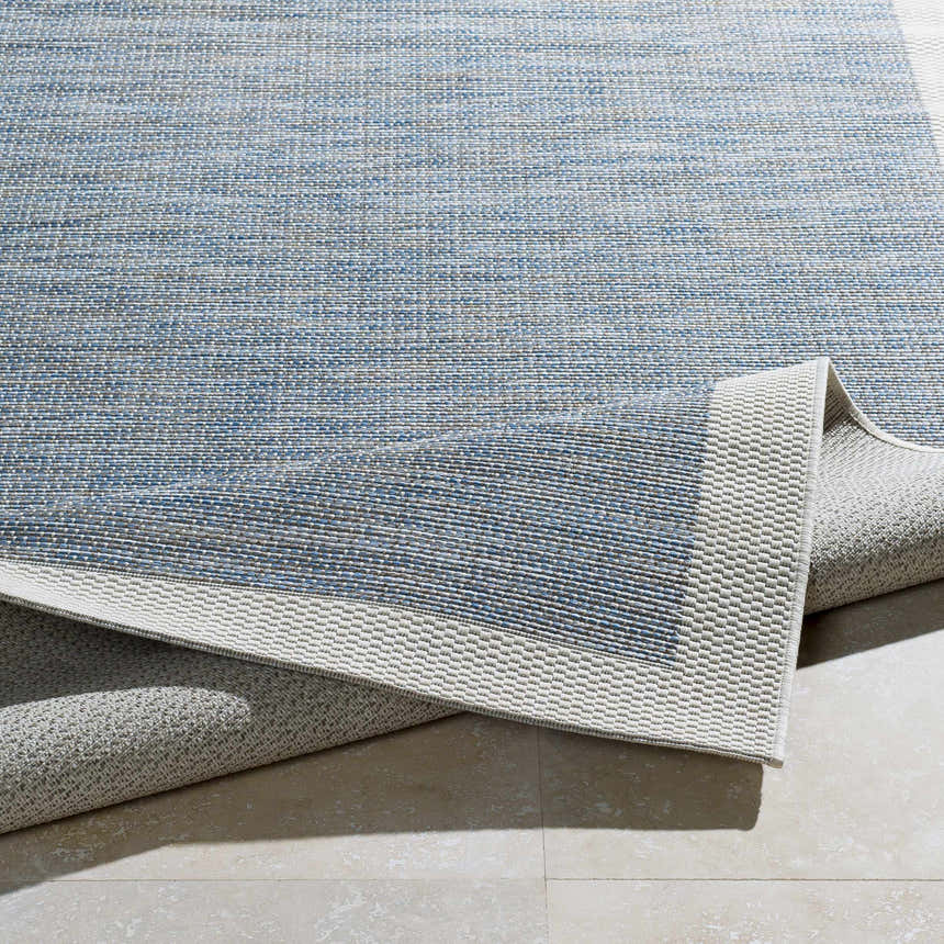 Close-up of the blue, cream, and taupe woven texture of the Wishon Area Rug. Neutral border detail. Fold